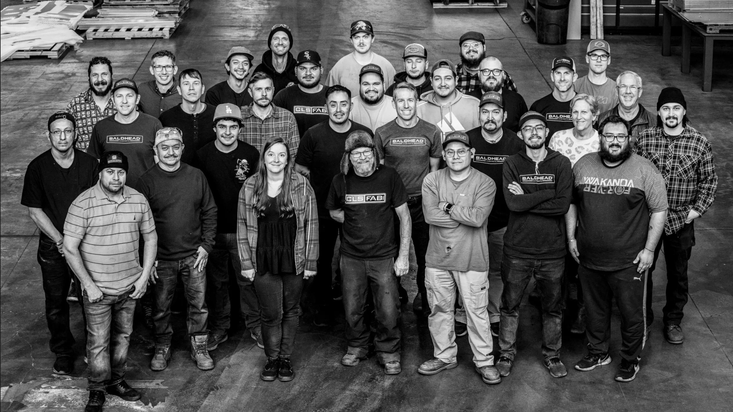 A group photo of the team at Baldhead Cabinets, a company specializing in custom metal cabinets, showcasing the diverse group of employees involved in the meticulous manufacture of high-quality cabinets for tools. The image captures the team in a workshop setting, emphasizing their collaborative spirit and dedication to craftsmanship.