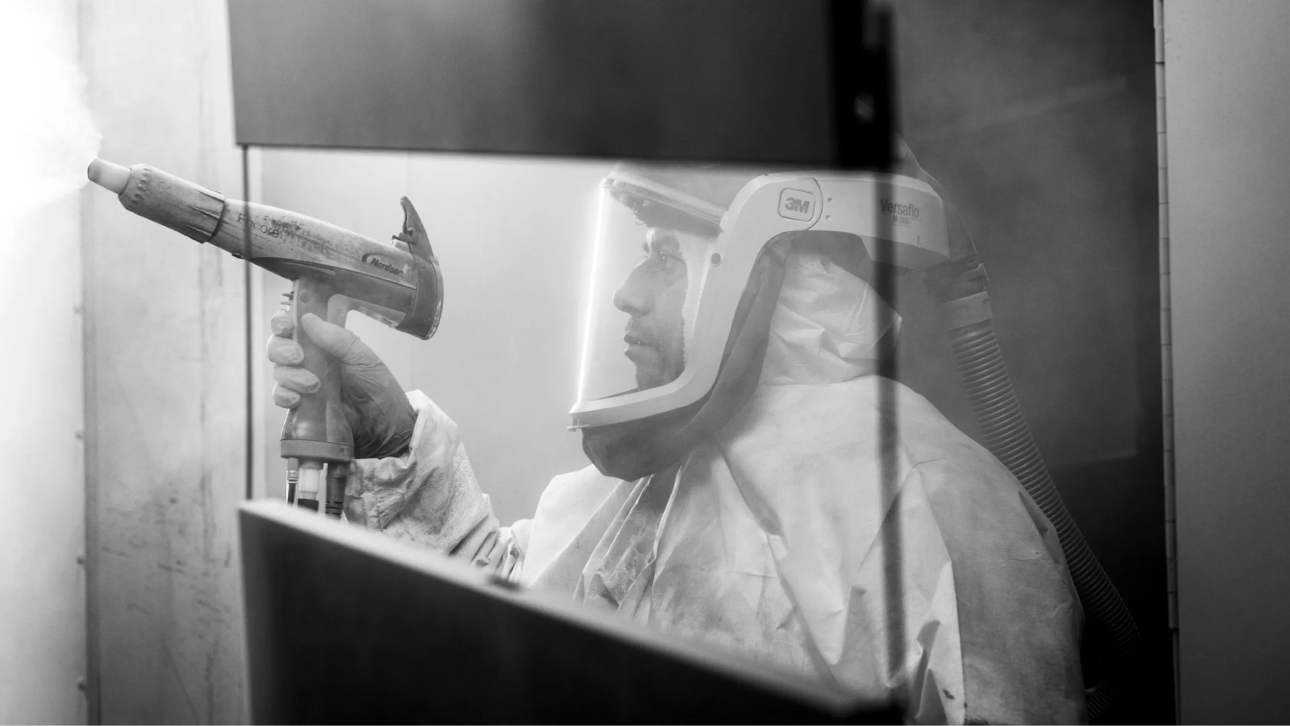 A person in protective gear meticulously operating a spray gun in a controlled environment, involved in the manufacture of custom metal cabinets. The scene emphasizes the process of creating high-quality cabinets for tools, showcasing precision and care in the production.