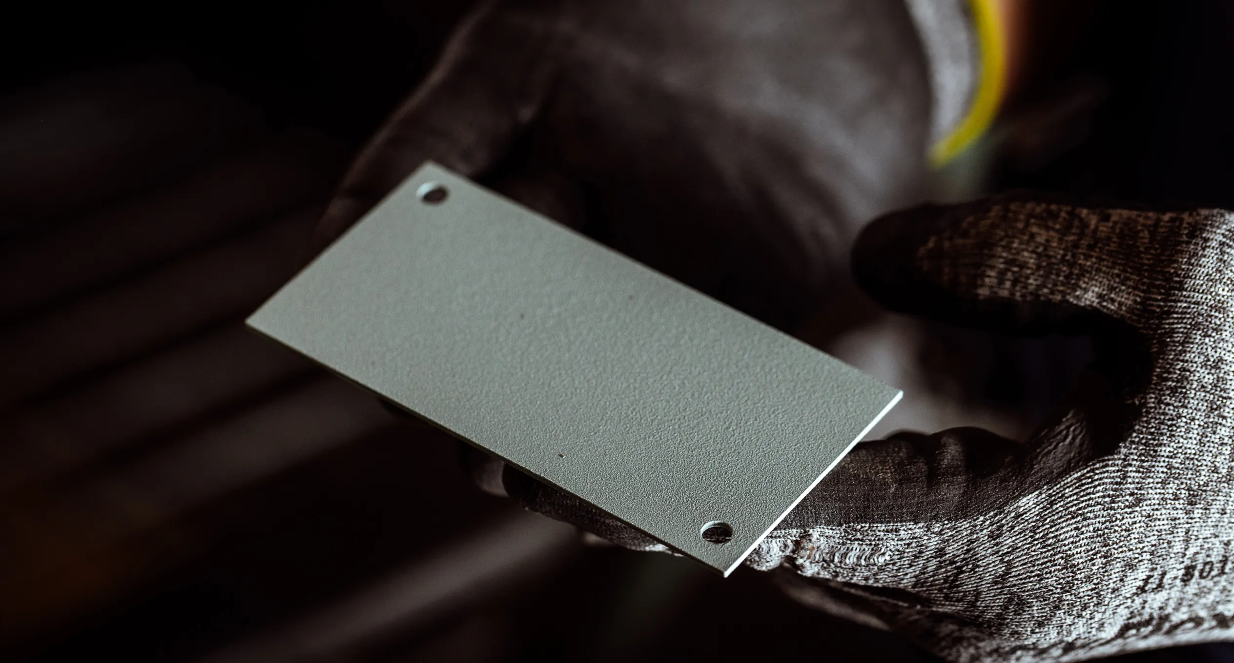 Person holding a metal sheet with two holes, wearing protective gloves.